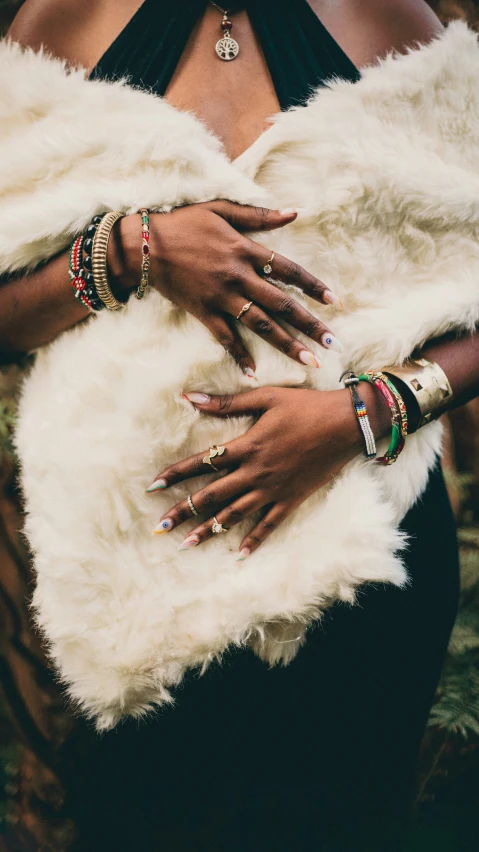 close up of hands wearing rings and holding onto a white fur coat