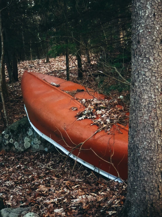 an orange canoe sitting on the ground in a forest