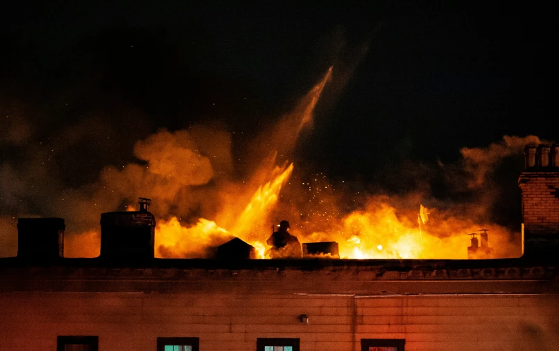 a fire with flames burning behind two large buildings