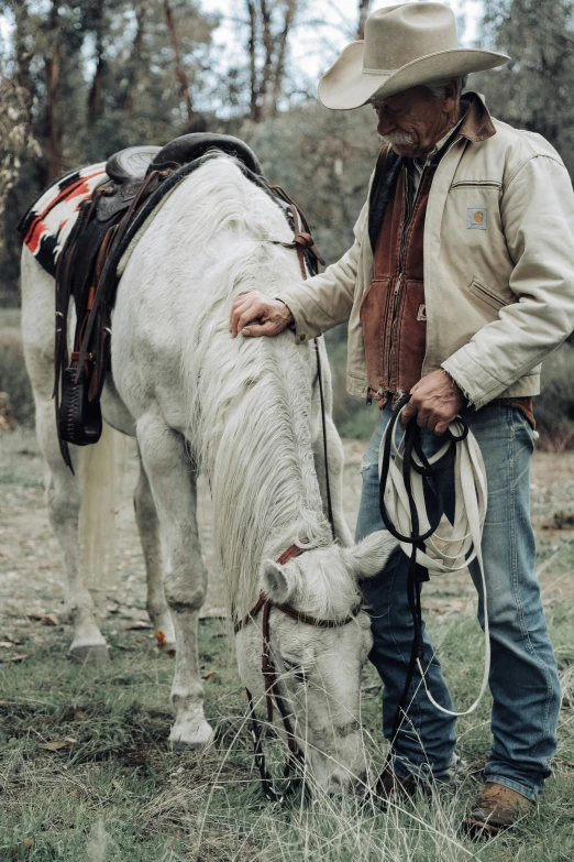 a man with a hat and cowboy wear on and his horse grazes