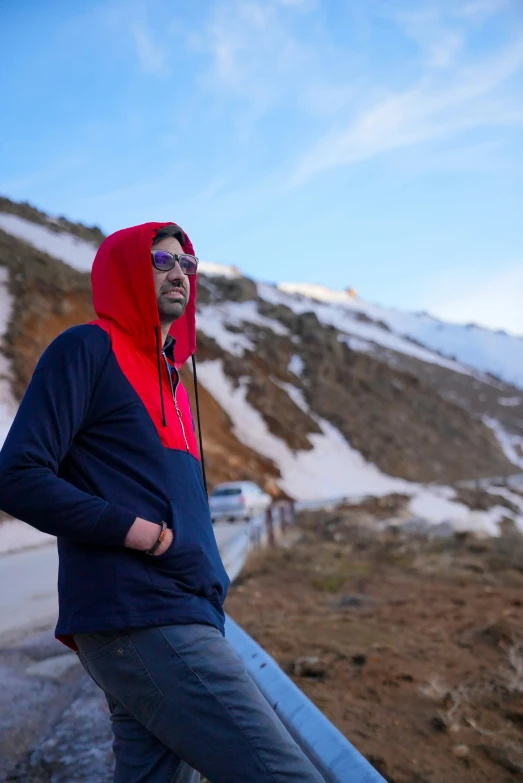 a man with sunglasses and hood on standing in front of mountains