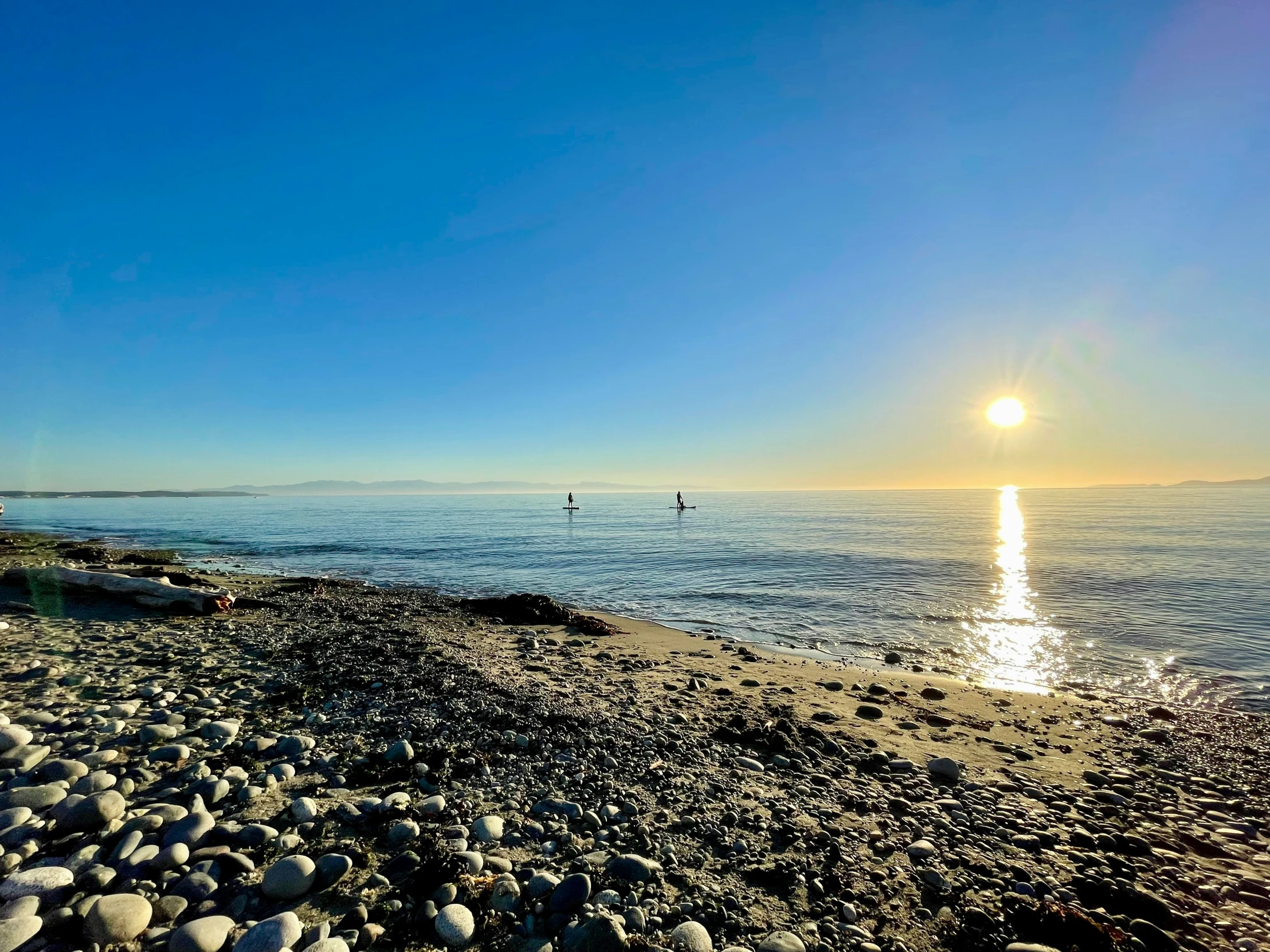 the sun rises over the beach and some rocks