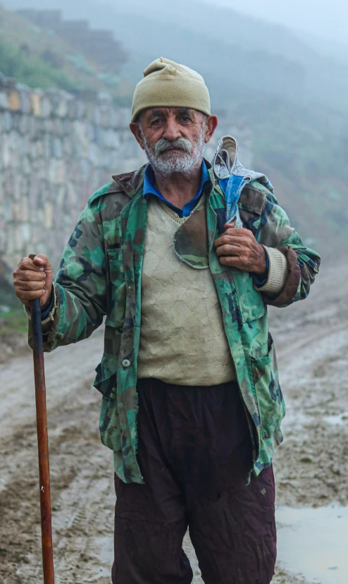 man with hat and jacket, holding a hiking stick in the middle of muddy path