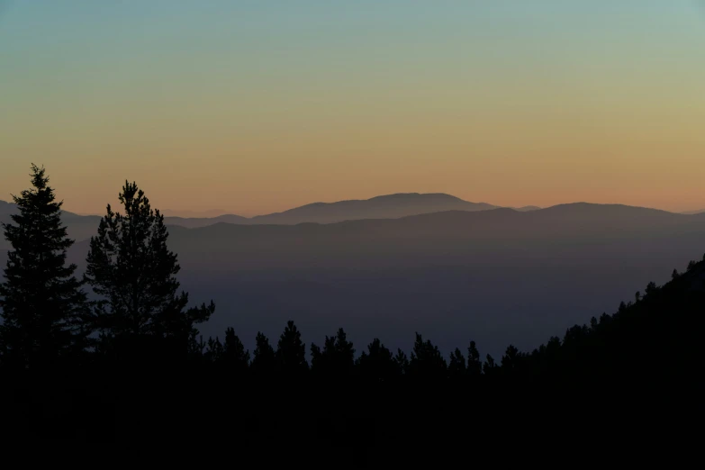 a silhouette view of the trees and the mountains at sunrise