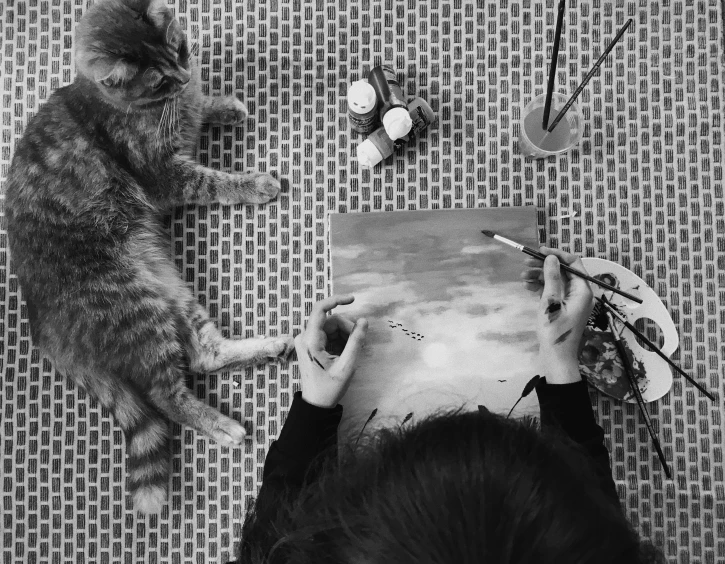 two cats sit on top of a man's head while he draws on a piece of paper