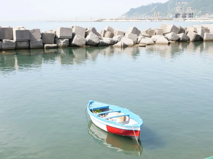 a small red and blue boat sitting in water next to rock piers