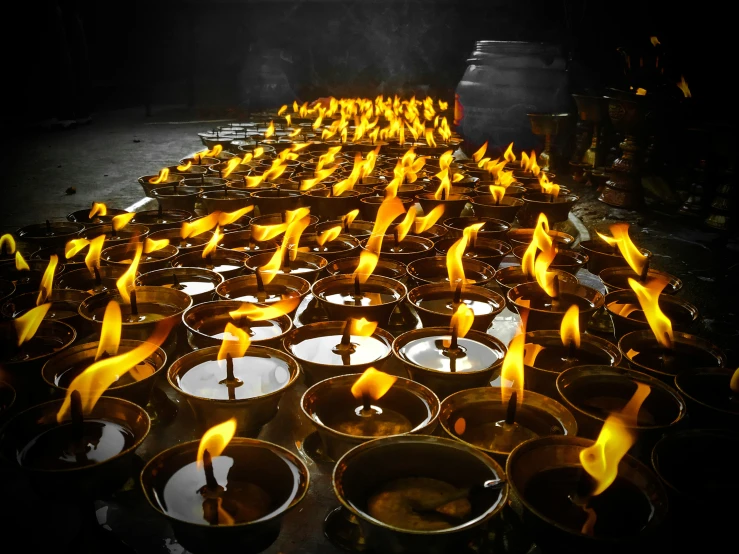 many candles in large metal cups that are lit