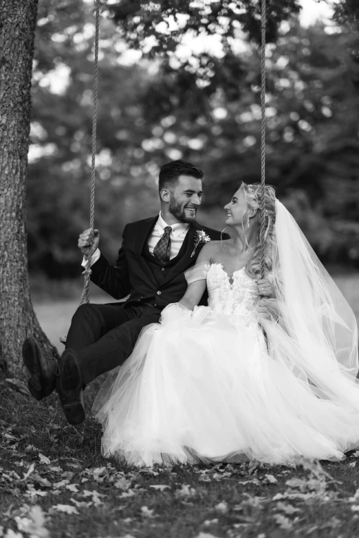 a bride and groom are sitting on the tree swing