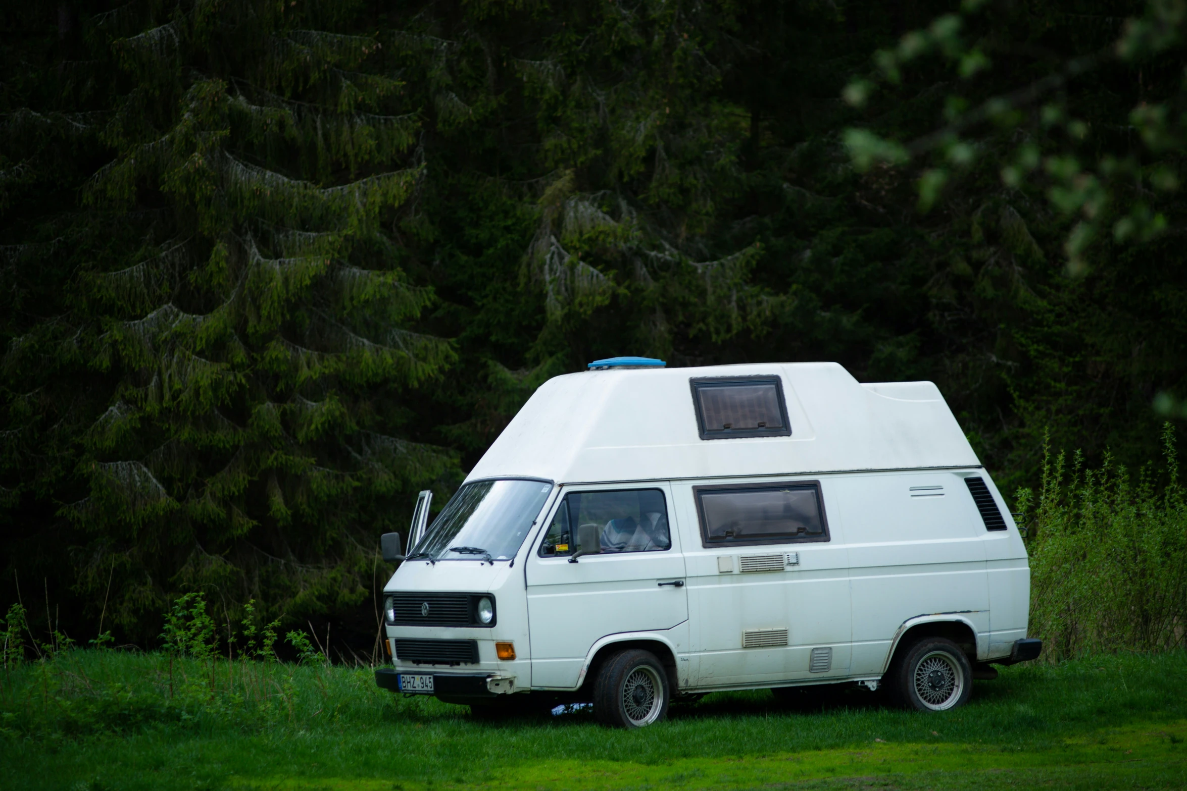 an rv parked on the grass with a forest in the background