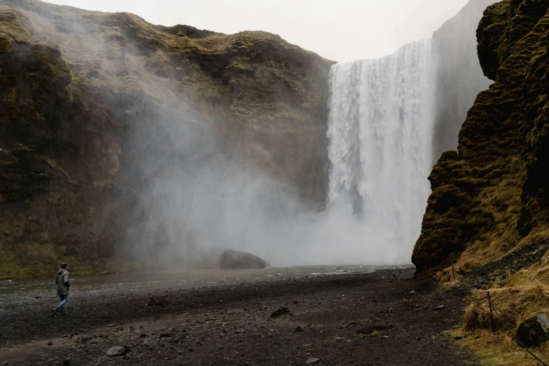 man standing in front of waterfall and running towards camera