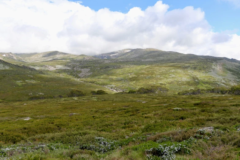 mountain side with some grass on the top and several hills with grass in the background