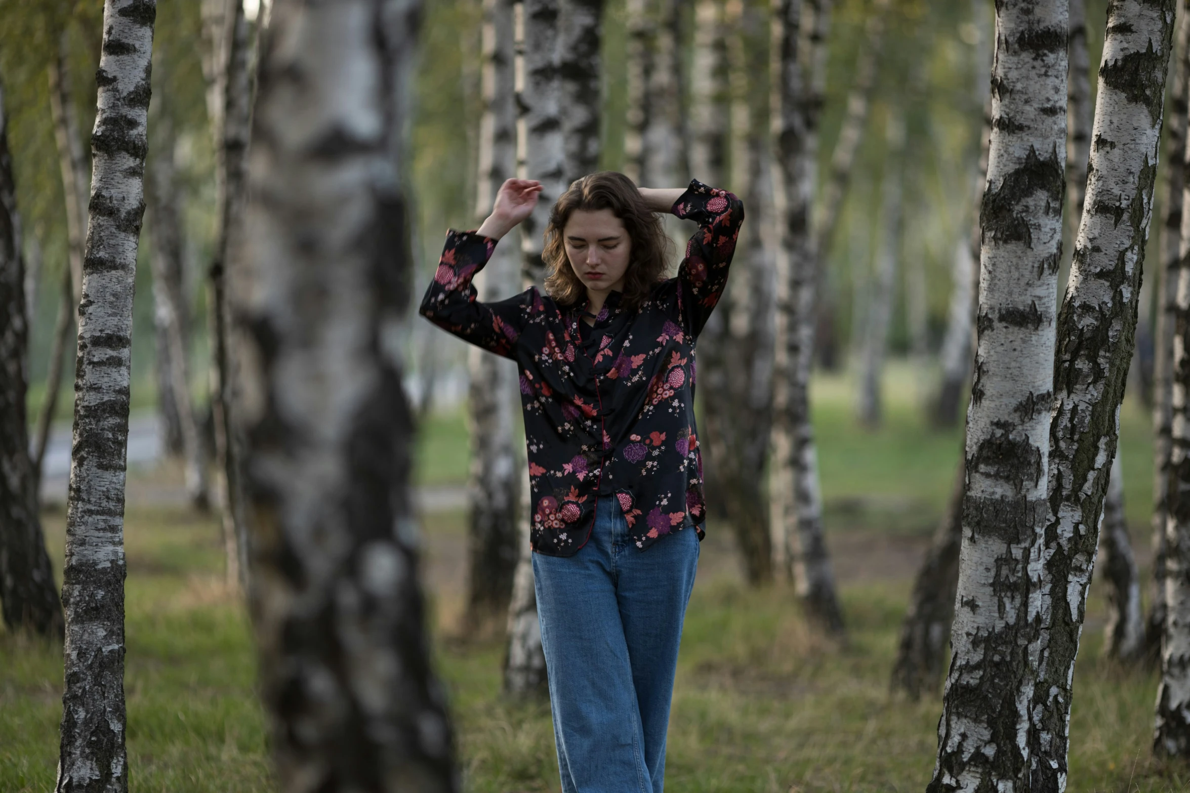 a woman stands between tall trunks of trees