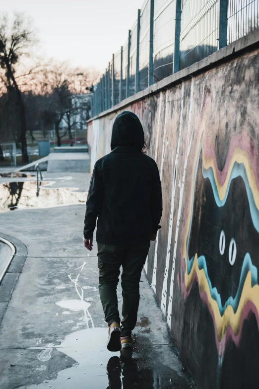 person wearing jacket walking down side of wall covered in graffiti