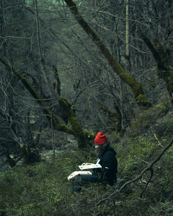 a woman in black jacket sitting on grass in a forest