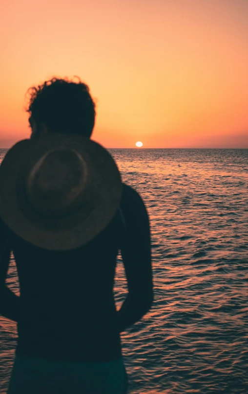 a woman is standing with her back to the camera and watching a sunset on the water