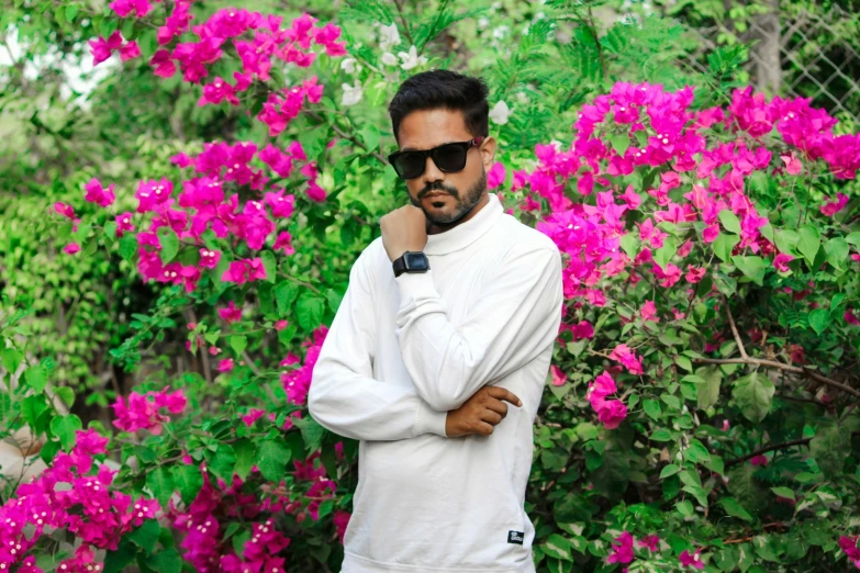 a man wearing glasses stands in front of some pretty flowers