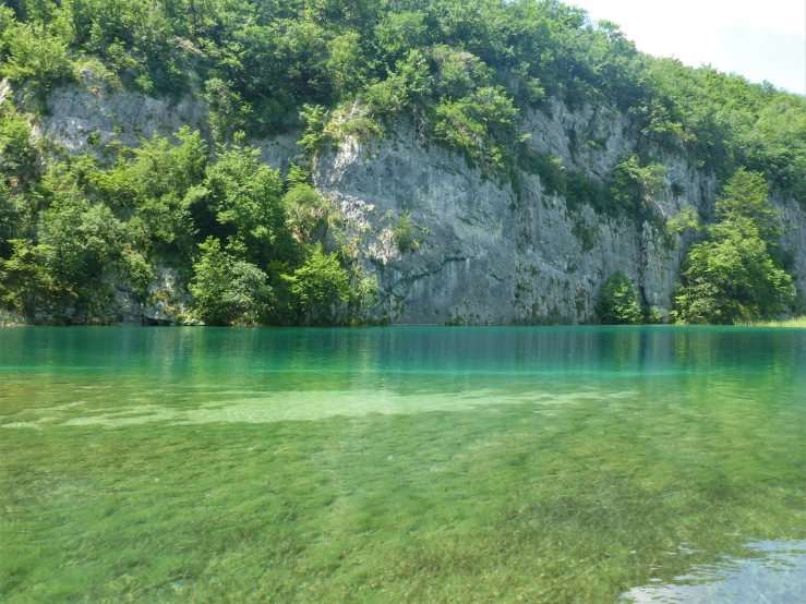 clear green water with trees surrounding it and mountains