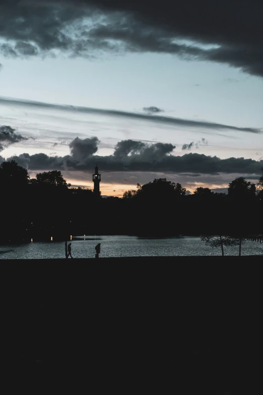 people sitting on a bench at sunset near a pond