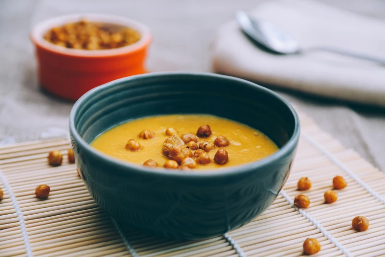 two bowls are on a mat and one is filled with soup