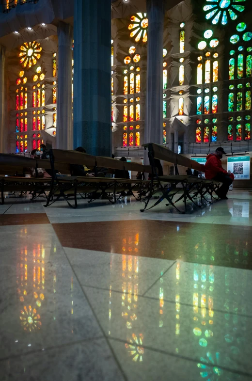 a large building has stained glass and a few people sitting at benches