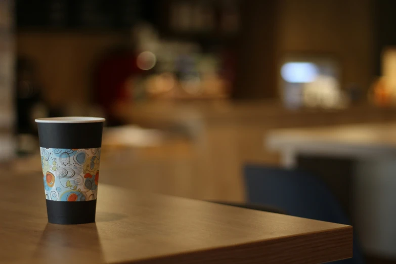 a black cup with a colorful painting on it sitting on a counter