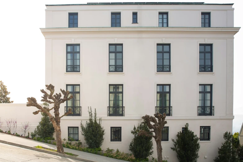 an apartment building with trees in front and cars parked on the street behind it