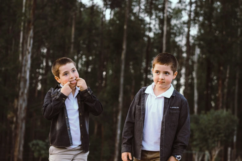 two boys standing next to each other with trees in the background