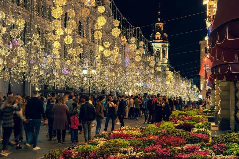 people walk down a city street decorated with christmas lights