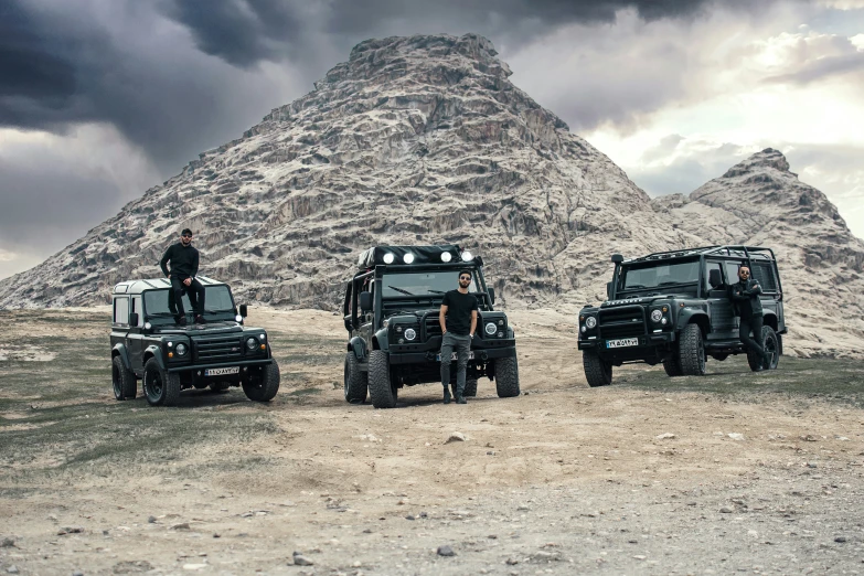 four military vehicles with two guys standing on them and one sitting on the roof