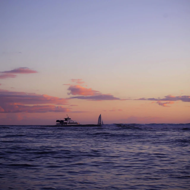 a small boat travels along in the ocean during sunset