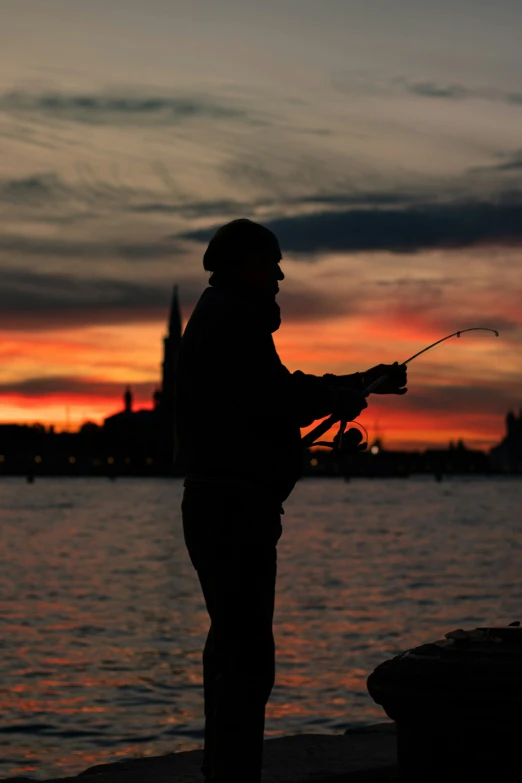 a man fishing from the shore at sunset