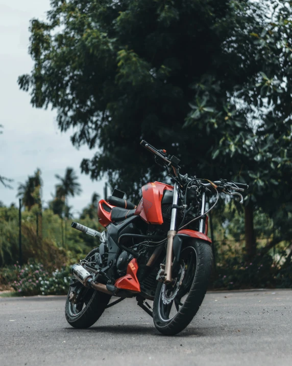 a red motorcycle parked on a street next to some trees