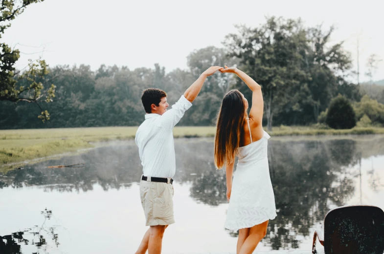 a couple holds their hands in the air near a body of water