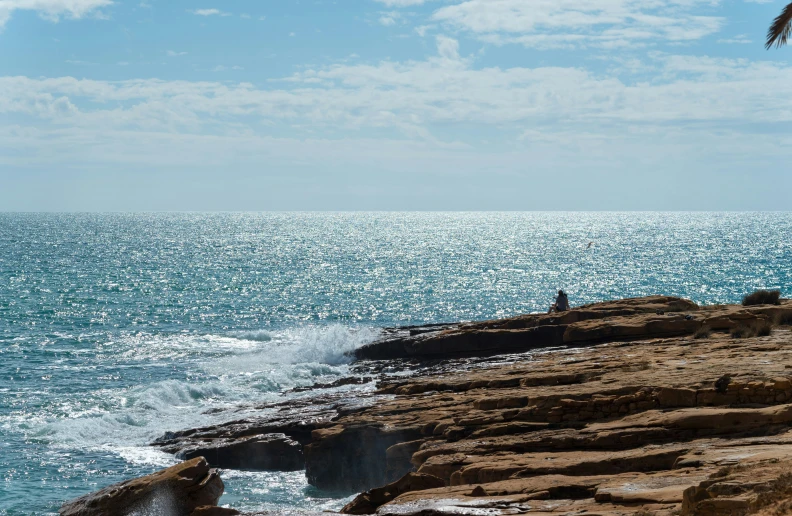 person sitting on a cliff overlooking the ocean