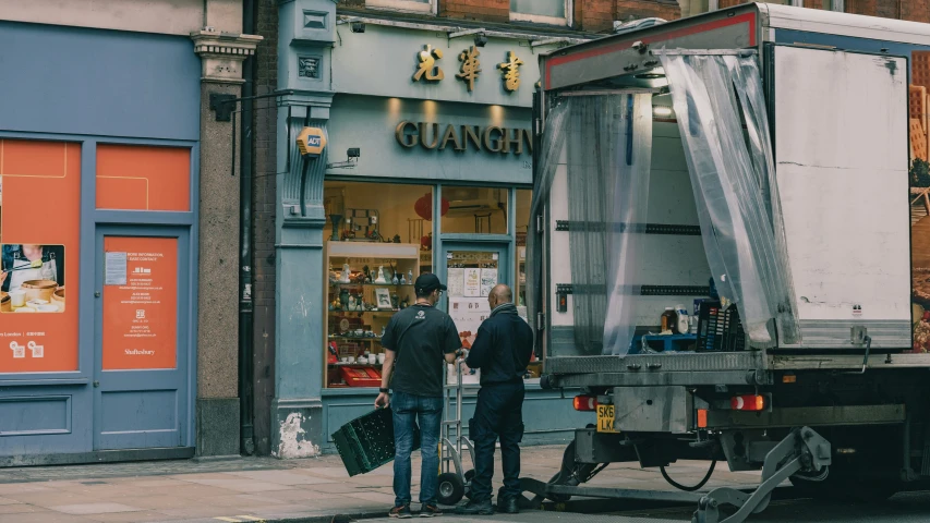 two men standing outside of a truck near a building