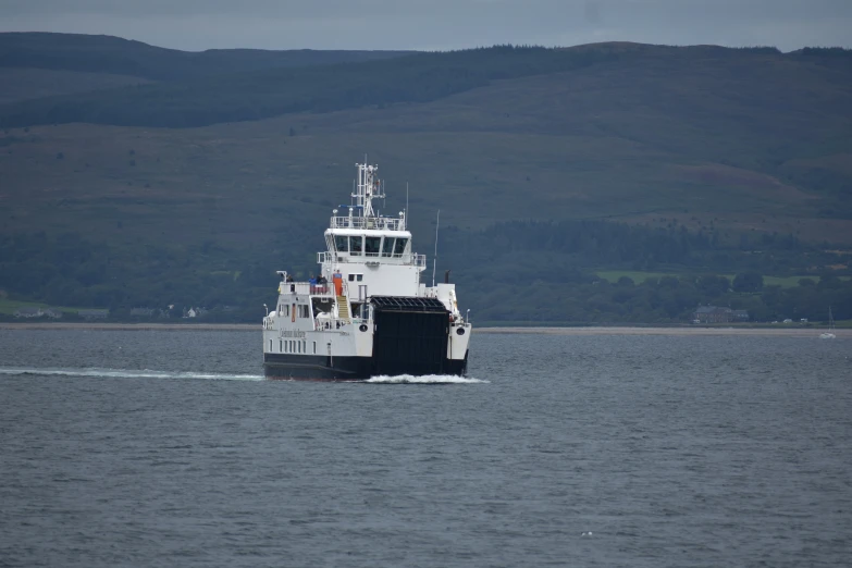 a large boat floating across a body of water near a hillside