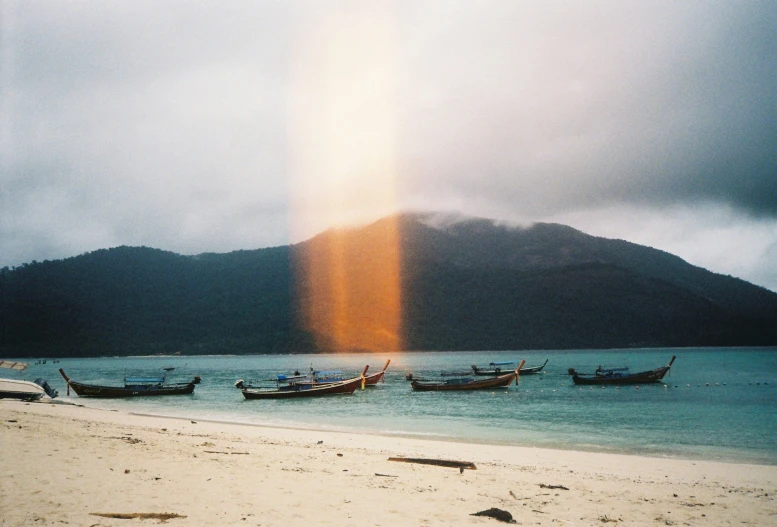 three boats moored at an empty beach with mountains in the background