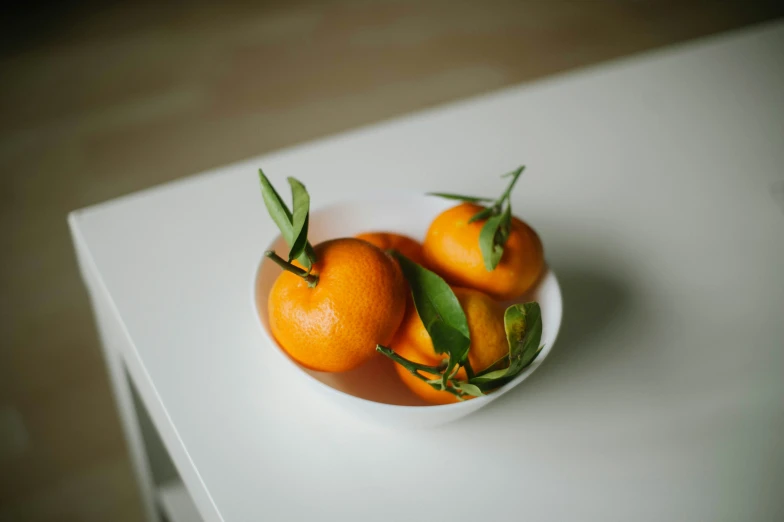 three oranges in a white bowl on a counter top