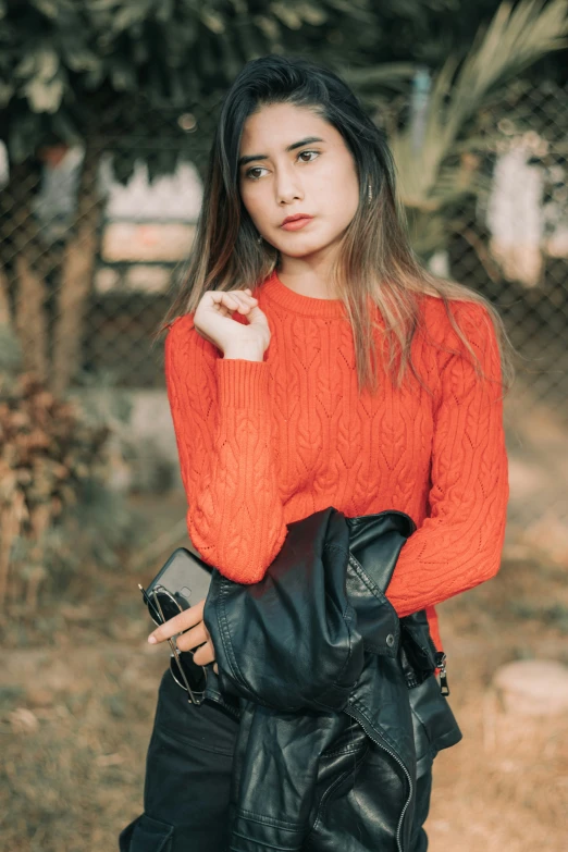 a woman in an orange sweater holding a purse