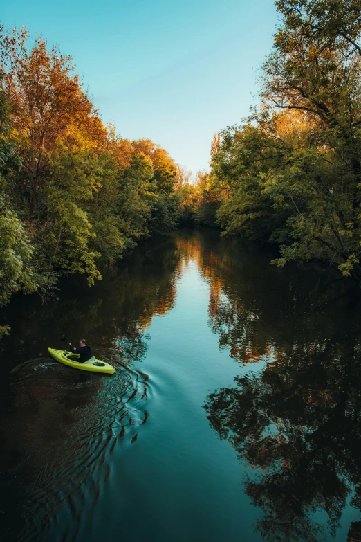 the person in a yellow kayak floats down a narrow river