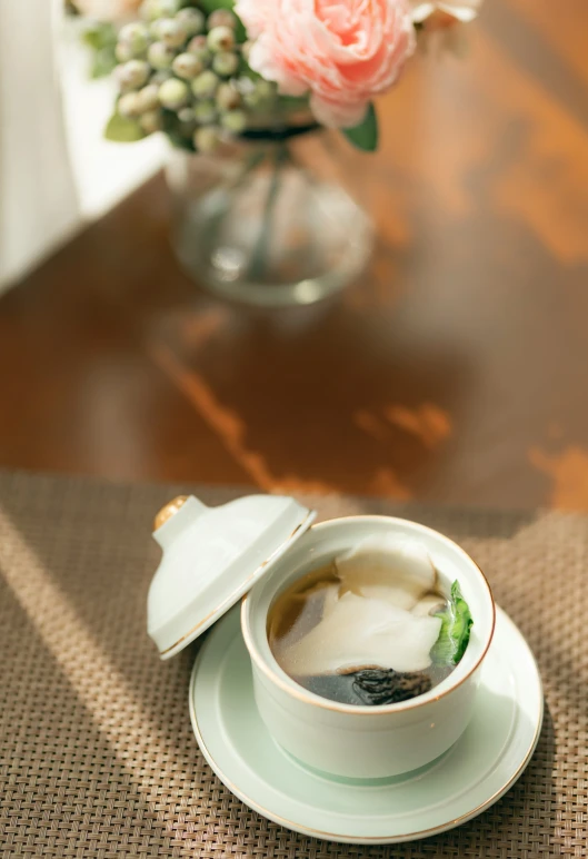 a plate on a table with a bowl of soup and saucer next to flowers