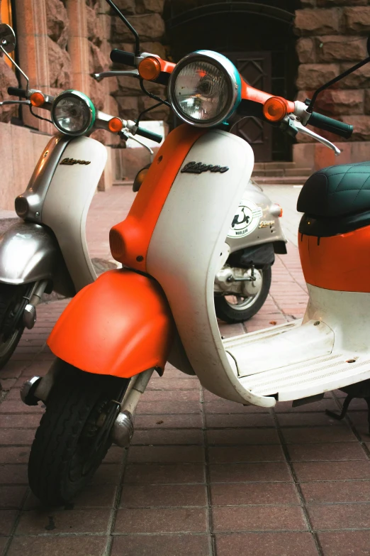 this is an orange and white vespa parked on a stone sidewalk