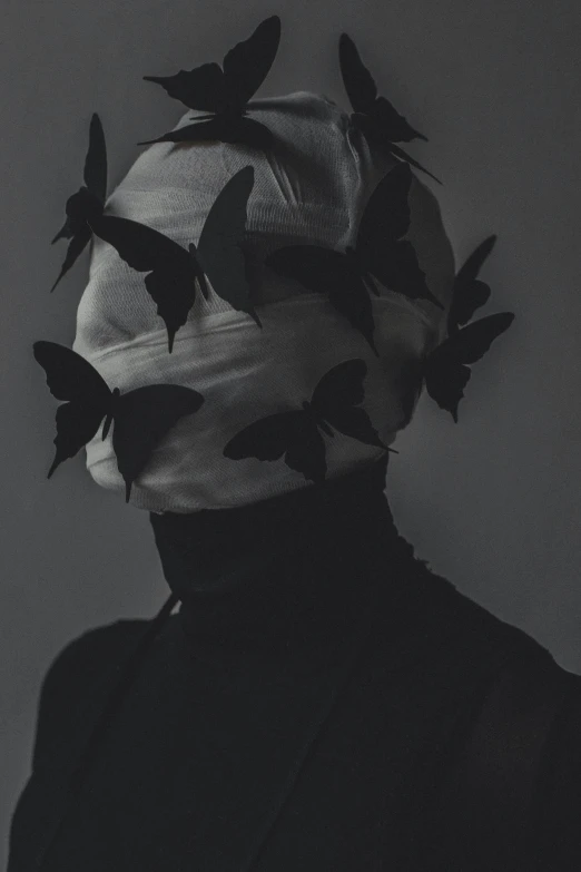 a black and white image of a man wearing a mask filled with erflies