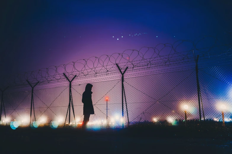 a man standing next to a barbed wire fence with the night sky behind him