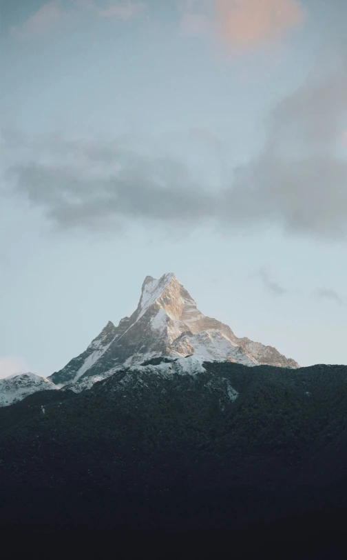 a very tall mountain covered in snow under a cloudy sky