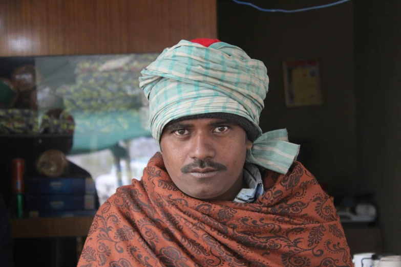 a man with a turban and a silly mustache is wearing a red paisley cape