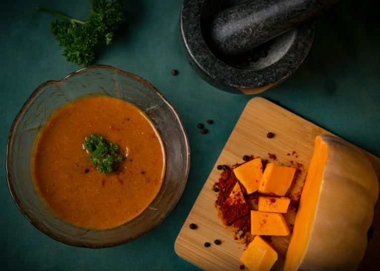 soup in a bowl, next to cheese blocks and a piece of broccoli