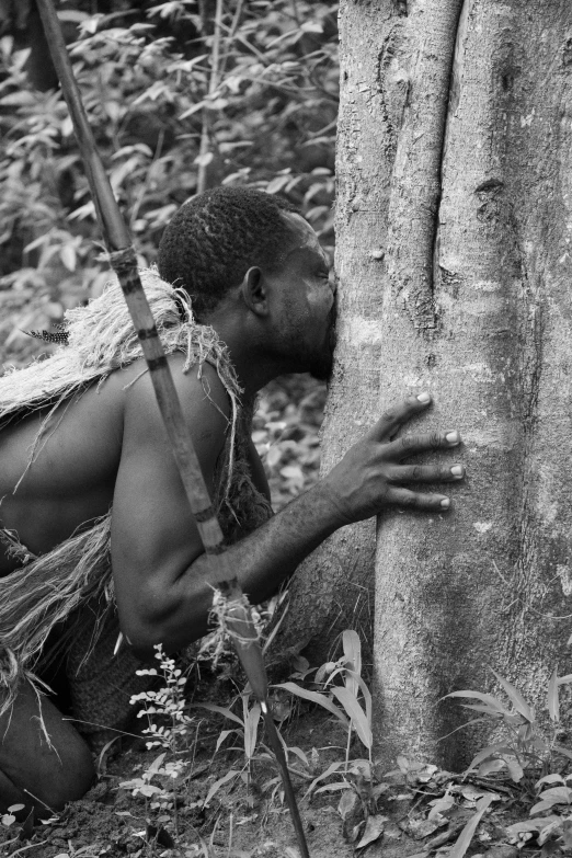 a man leaning against a tree while crouching next to it