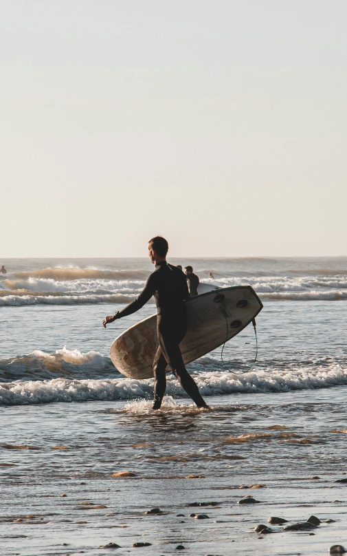 a man walking along a beach holding a surf board