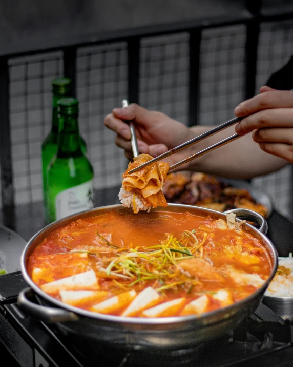 two people holding chopsticks over a large pan with food